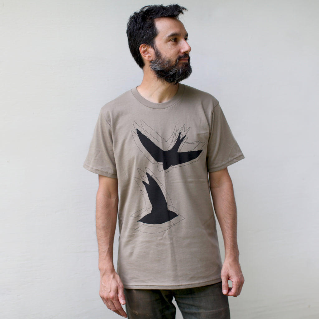 A male model looking to the right wearing a light brown t-shirt with 2 flying birds on the front.