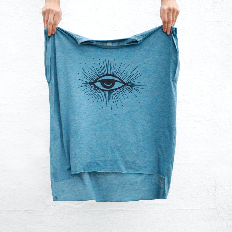 A pair of hands holding a women's deep teal muscle tee with a protective symbol third eye of Horus design hand printed on the front.